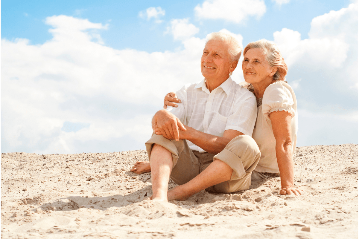 An elderly couple sitting on the beach looking at the water